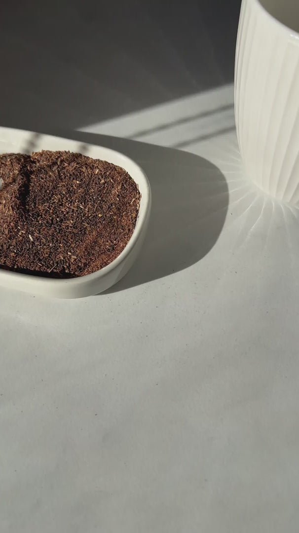 Karobe tasting ritual: a hand lifts a glass of roasted carob drink, bringing it close to the camera to reveal its rich texture and dark color.